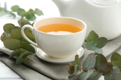 Photo of Aromatic tea in cup and eucalyptus branches on table, closeup