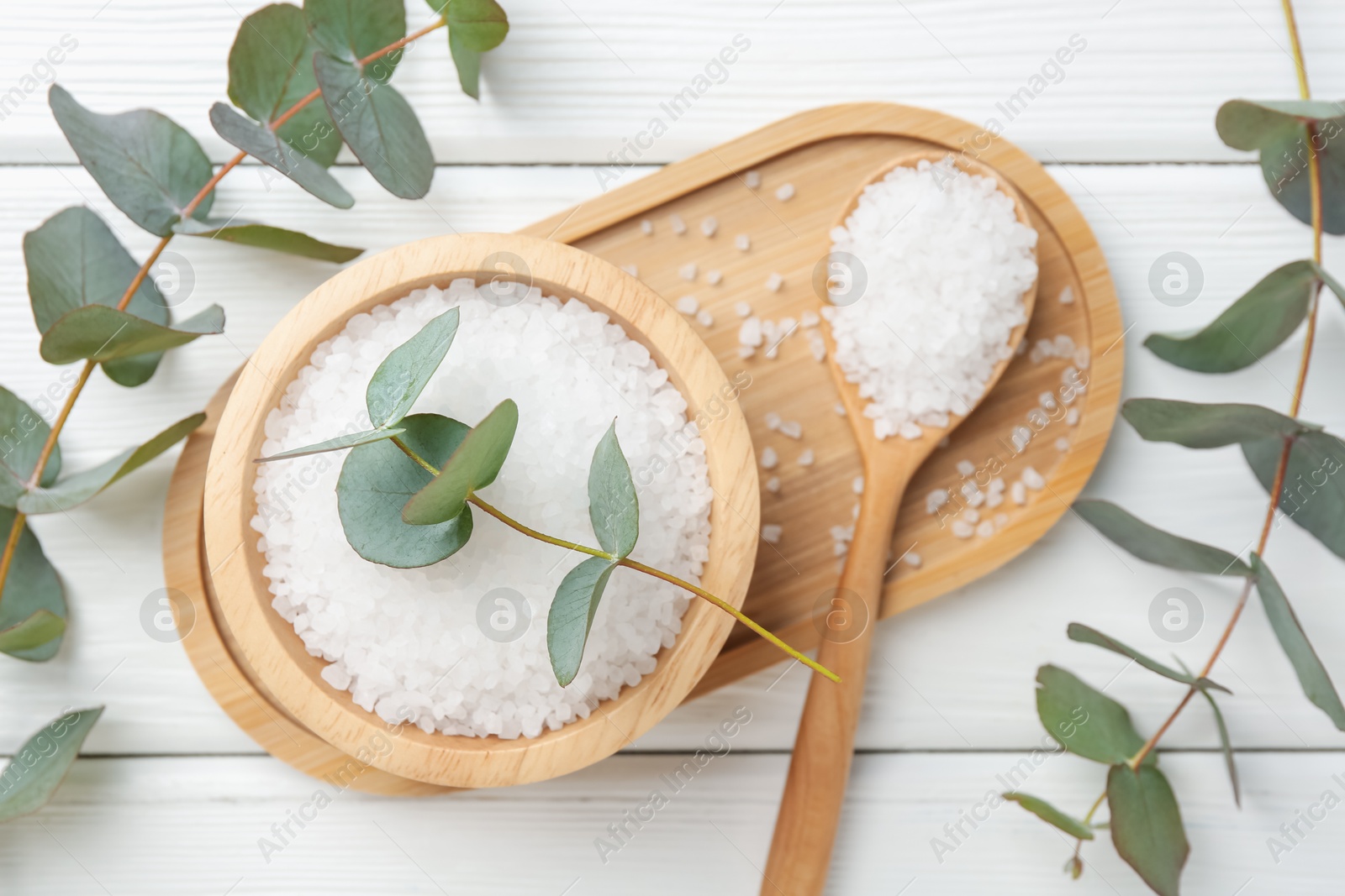 Sea salt and beautiful eucalyptus branches on white wooden table, flat lay Photo of Sea salt and beautiful eucalyptus branches on white wooden table, flat lay