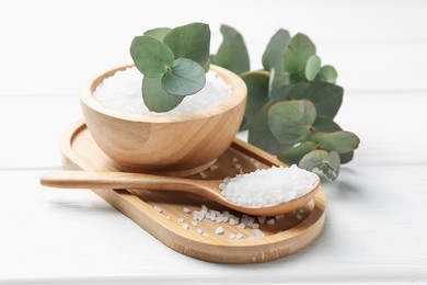 Photo of Sea salt and beautiful eucalyptus branches on white wooden table, closeup