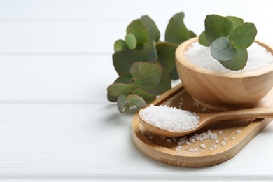 Photo of Sea salt and beautiful eucalyptus branches on white wooden table, closeup. Space for text