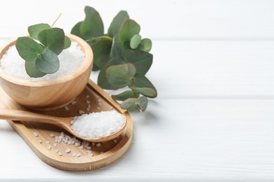 Photo of Sea salt and beautiful eucalyptus branches on white wooden table, closeup. Space for text