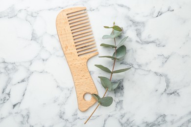 Photo of Comb and eucalyptus branch on white marble table, flat lay