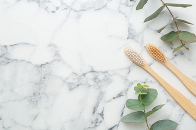 Photo of Bamboo toothbrushes and eucalyptus branches on white marble table, flat lay. Space for text