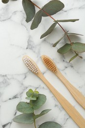 Photo of Bamboo toothbrushes and eucalyptus branches on white marble table, flat lay
