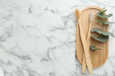 Photo of Bamboo toothbrushes and eucalyptus branch on white marble table, top view. Space for text