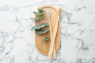 Photo of Bamboo toothbrushes and eucalyptus branch on white marble table, top view