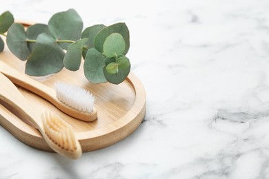 Photo of Bamboo toothbrushes and eucalyptus branch on white marble table, closeup. Space for text