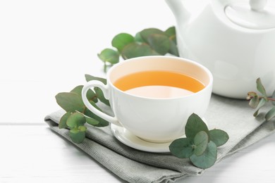 Photo of Aromatic tea in cup and eucalyptus branches on white wooden table, closeup