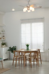 Photo of Wooden table, chairs, tulips and green houseplants near window indoors. Interior design