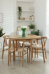 Photo of Wooden table, chairs, tulips and green houseplants indoors. Interior design