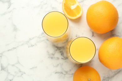 Photo of Orange juice in glasses and fresh fruits on white marble table, flat lay. Space for text