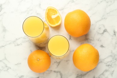 Photo of Orange juice in glasses and fresh fruits on white marble table, flat lay