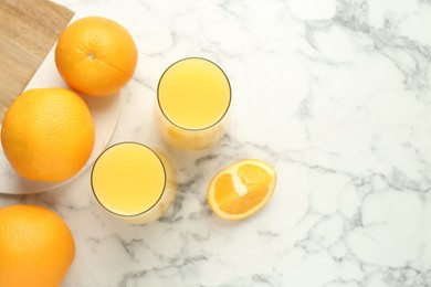 Photo of Orange juice in glasses and fresh fruits on white marble table, flat lay. Space for text
