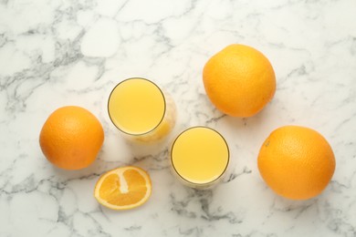 Photo of Orange juice in glasses and fresh fruits on white marble table, flat lay