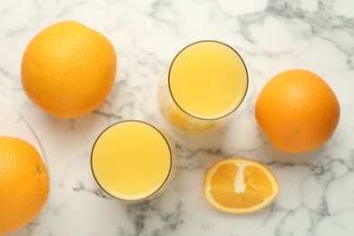 Photo of Orange juice in glasses and fresh fruits on white marble table, flat lay