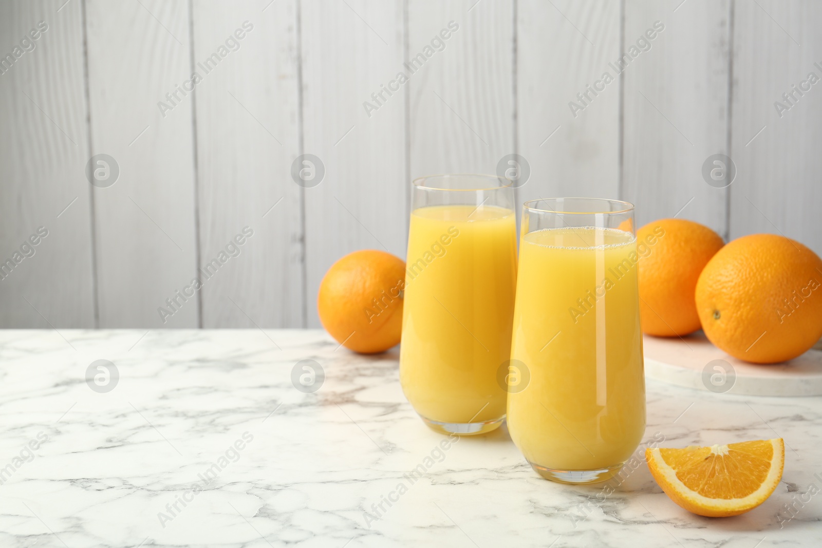 Orange juice in glasses and fresh fruits on white marble table, space for text Photo of Orange juice in glasses and fresh fruits on white marble table, space for text