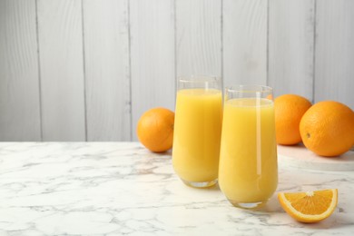 Photo of Orange juice in glasses and fresh fruits on white marble table, space for text