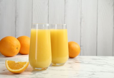 Photo of Orange juice in glasses and fresh fruits on white marble table, space for text