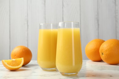 Photo of Orange juice in glasses and fresh fruits on white marble table, closeup