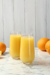 Photo of Orange juice in glasses and fresh fruits on white marble table