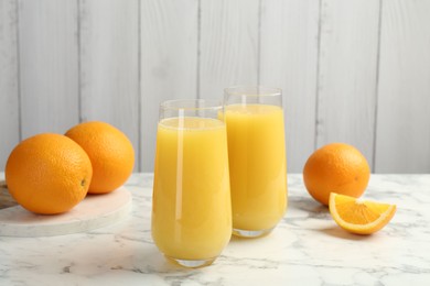 Photo of Orange juice in glasses and fresh fruits on white marble table