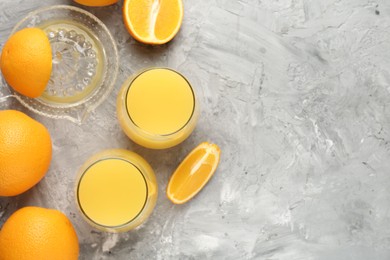 Photo of Orange juice in glasses, fresh fruits and juicer on grey table, flat lay. Space for text