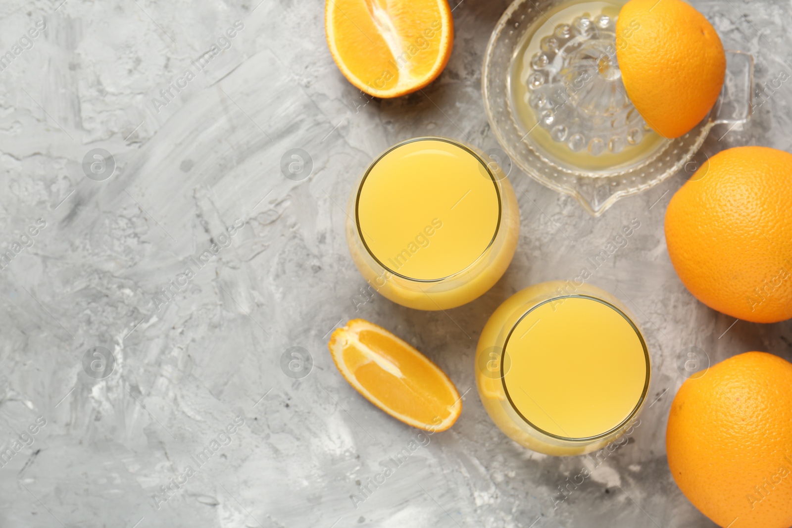 Orange juice in glasses, fresh fruits and juicer on grey table, flat lay. Space for text Photo of Orange juice in glasses, fresh fruits and juicer on grey table, flat lay. Space for text