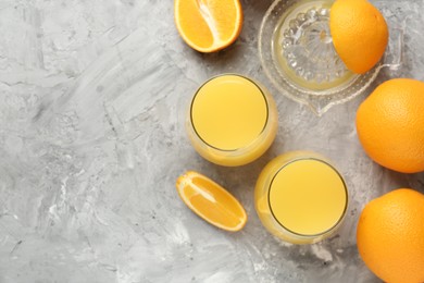 Photo of Orange juice in glasses, fresh fruits and juicer on grey table, flat lay. Space for text