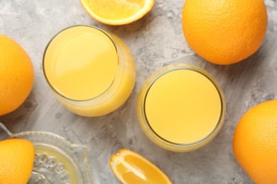 Photo of Orange juice in glasses, fresh fruits and juicer on grey table, flat lay