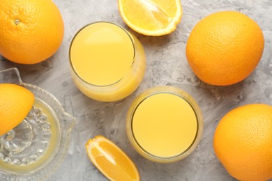 Photo of Orange juice in glasses, fresh fruits and juicer on grey table, flat lay