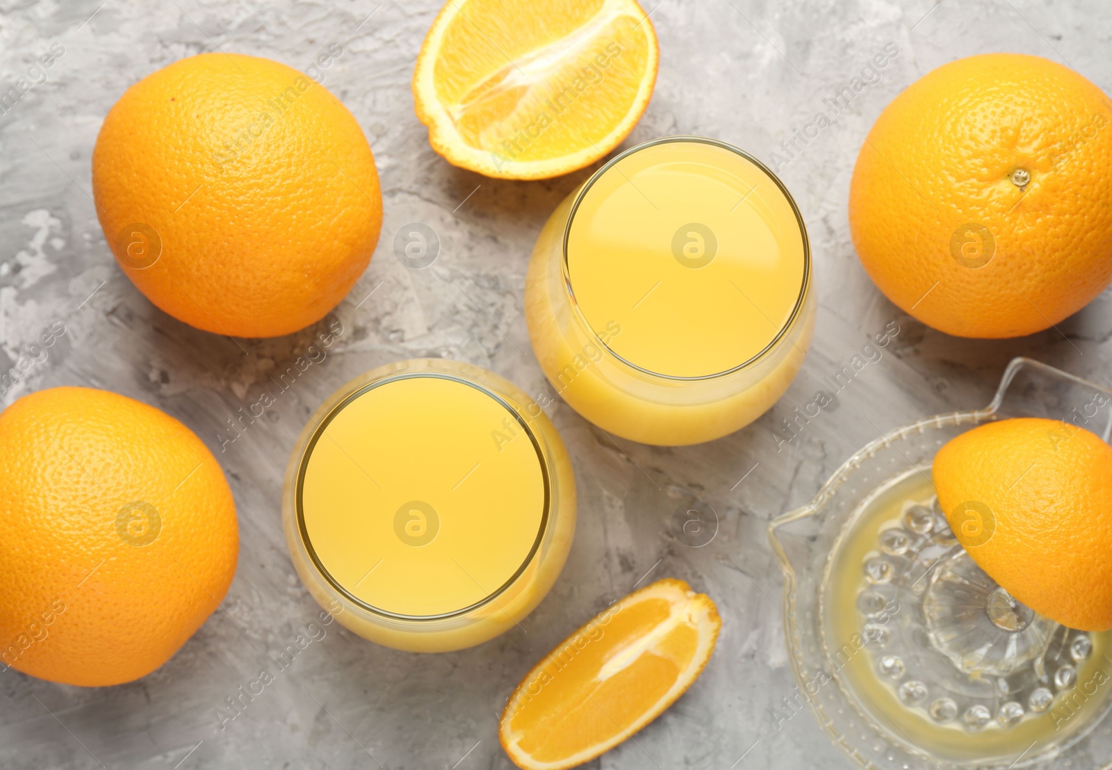 Orange juice in glasses, fresh fruits and juicer on grey table, flat lay Photo of Orange juice in glasses, fresh fruits and juicer on grey table, flat lay