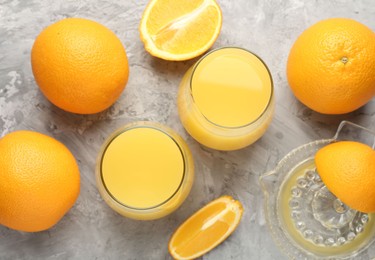 Photo of Orange juice in glasses, fresh fruits and juicer on grey table, flat lay