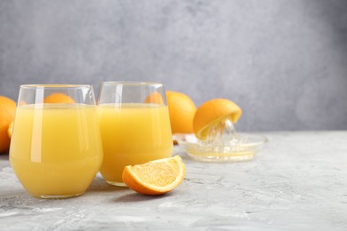 Photo of Orange juice in glasses, fresh fruits and juicer on grey table, closeup. Space for text