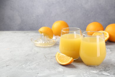 Photo of Orange juice in glasses, fresh fruits and juicer on grey table, space for text