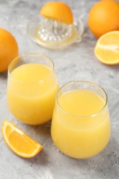 Photo of Orange juice in glasses, fresh fruits and juicer on grey table, closeup