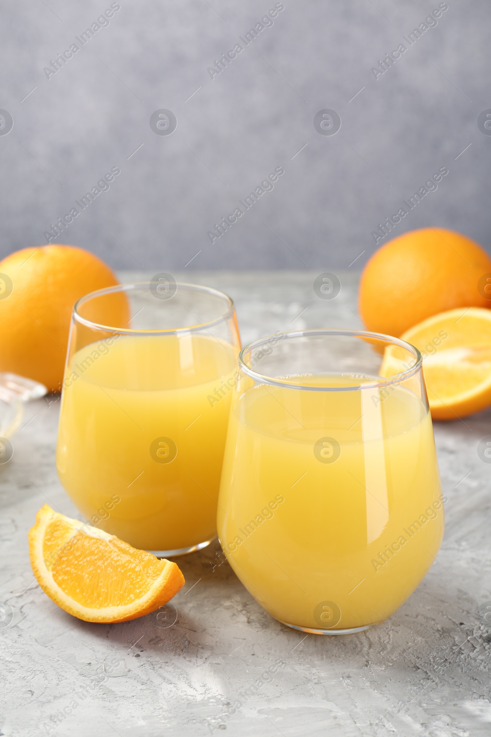 Orange juice in glasses and fresh fruits on grey table, closeup Photo of Orange juice in glasses and fresh fruits on grey table, closeup