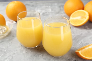 Photo of Orange juice in glasses and fresh fruits on grey table, closeup