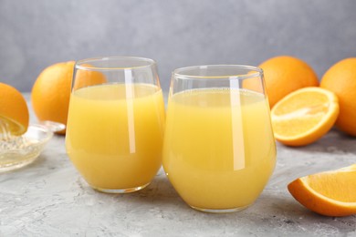 Photo of Orange juice in glasses and fresh fruits on grey table, closeup