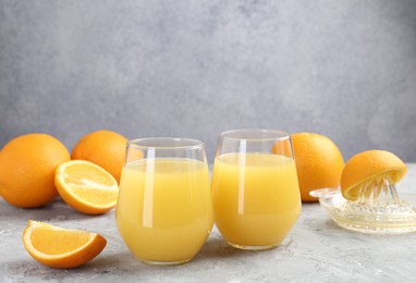 Photo of Orange juice in glasses, fresh fruits and juicer on grey table