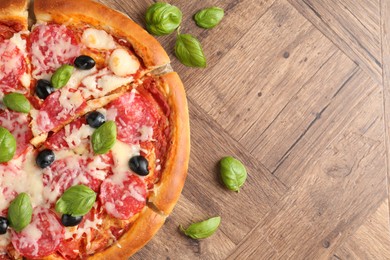 Photo of Tasty pizza with salami, cheese, basil and olives on wooden table, flat lay. Space for text