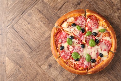 Photo of Tasty pizza with salami, cheese, basil and olives on wooden table, top view. Space for text