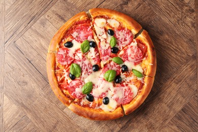 Photo of Tasty pizza with salami, cheese, basil and olives on wooden table, top view