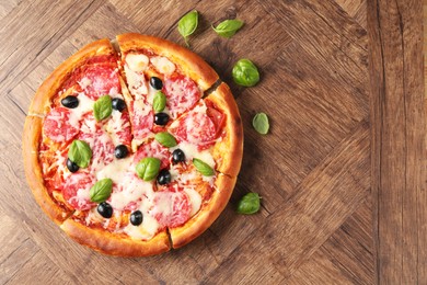 Photo of Tasty pizza with salami, cheese, basil and olives on wooden table, flat lay. Space for text