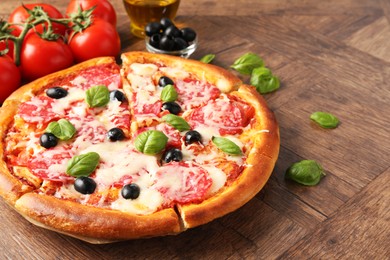 Photo of Tasty pizza and ingredients on wooden table, closeup. Space for text