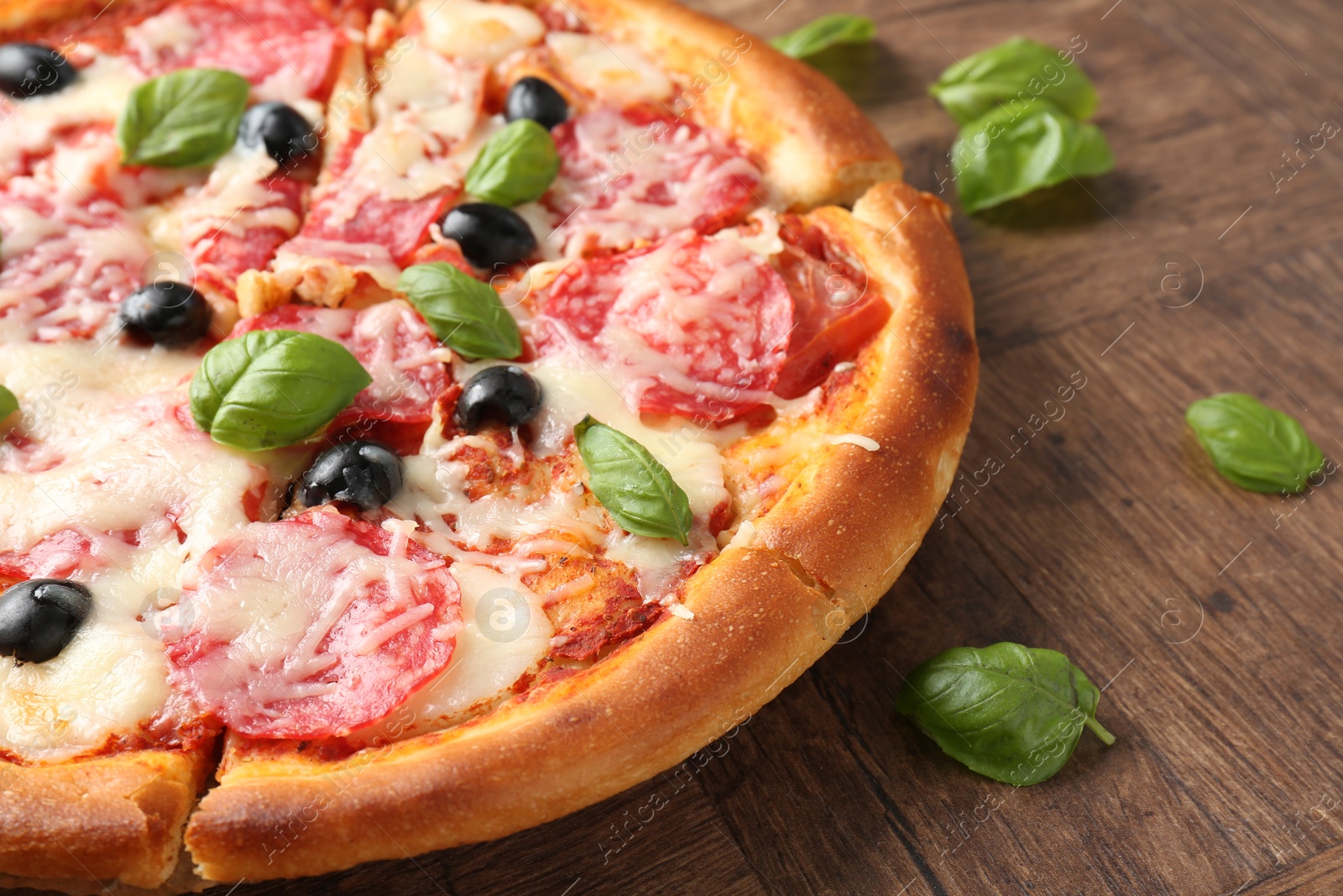 Photo of Tasty pizza with salami, cheese, basil and olives on wooden table, closeup