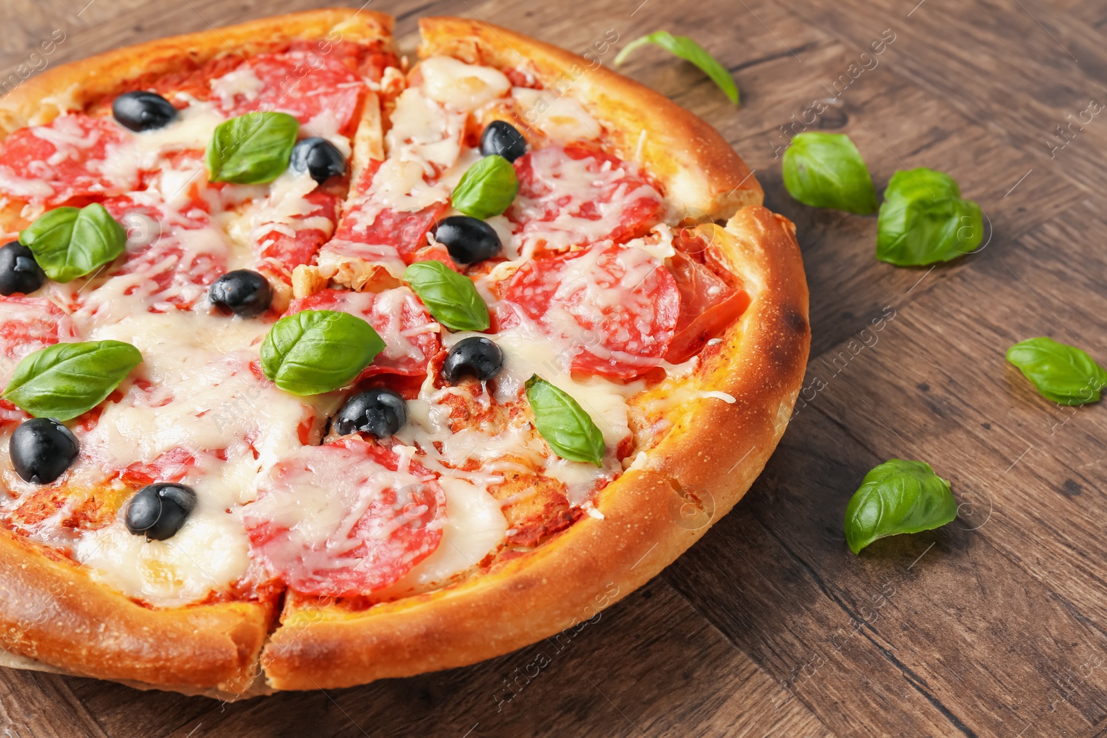 Tasty pizza with salami, cheese, basil and olives on wooden table, closeup Photo of Tasty pizza with salami, cheese, basil and olives on wooden table, closeup