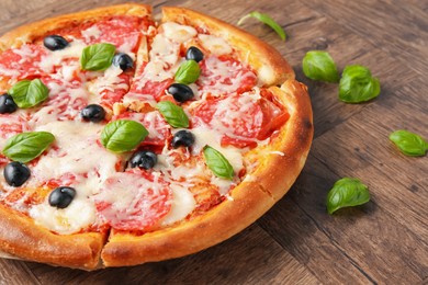 Photo of Tasty pizza with salami, cheese, basil and olives on wooden table, closeup