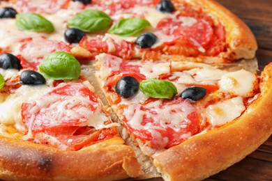 Photo of Tasty pizza with salami, cheese, basil and olives on table, closeup