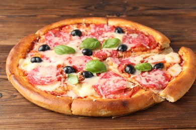 Photo of Tasty pizza with salami, cheese, basil and olives on wooden table, closeup