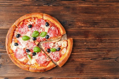 Photo of Tasty pizza with salami, cheese, basil and olives on wooden table, top view. Space for text